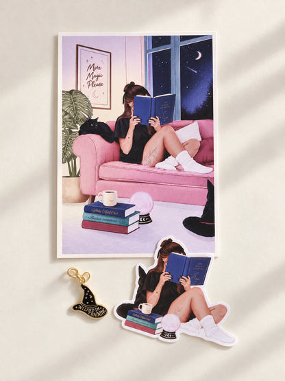 Pack de papelería ilustrada de Halloween con postal y sticker de una chica leyendo un libro mágico junto a un gato negro, y charm metálico de sombrero de bruja negro y dorado con la inscripción «Wizard in Training», sobre fondo crema.
